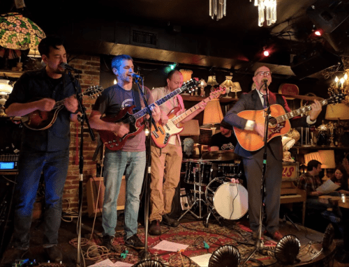 Four musicians perform on stage with various instruments in a lively, dimly lit venue.