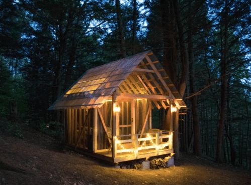 A cozy wooden cabin illuminated by warm lights, surrounded by trees at dusk.
