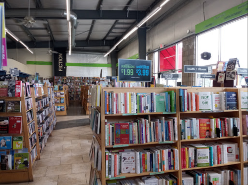 A spacious bookstore interior with wooden shelves filled with books, signs displaying prices, and a bright, inviting atmosphere.