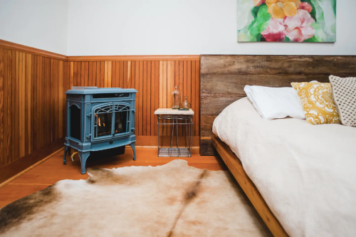 Cozy bedroom with a wooden bed, colorful artwork, a blue stove, and a cowhide rug on the floor.