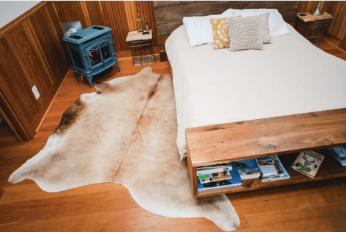 Cozy bedroom featuring a bed, wooden furniture, and a large cowhide rug on polished wooden floors.