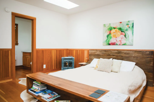 Cozy bedroom with a wooden bed, a coffee table, and a colorful painting on the wall, featuring warm wood accents.