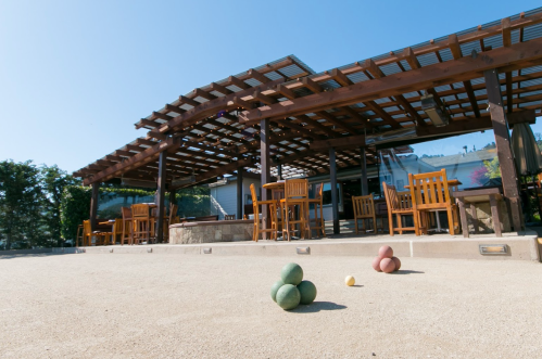 A sunny outdoor patio with wooden furniture and a bocce ball court featuring colorful balls on the ground.