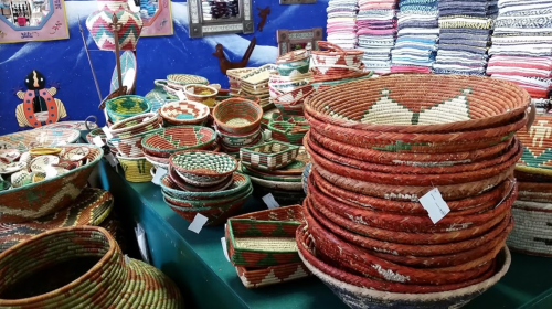 A colorful display of woven baskets in various shapes and sizes, arranged on a green table against a blue wall.