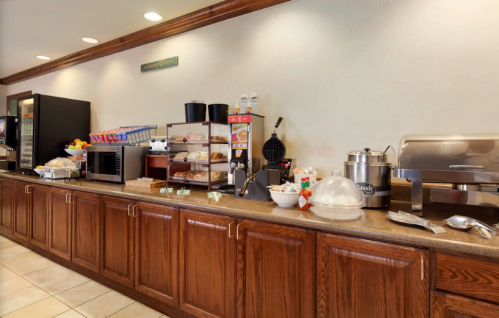 A buffet counter with a microwave, snacks, and a waffle maker in a well-lit dining area.