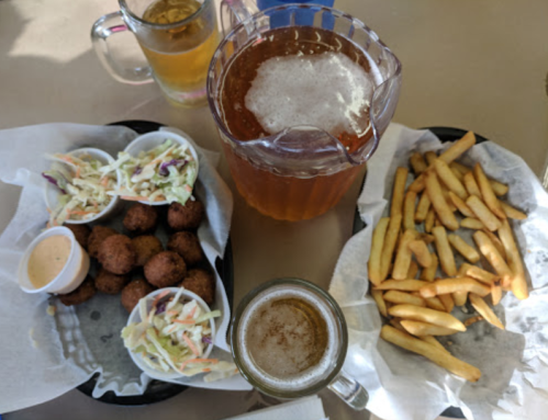 A table with a pitcher of iced tea, a glass of beer, fried food, coleslaw, and a plate of fries.