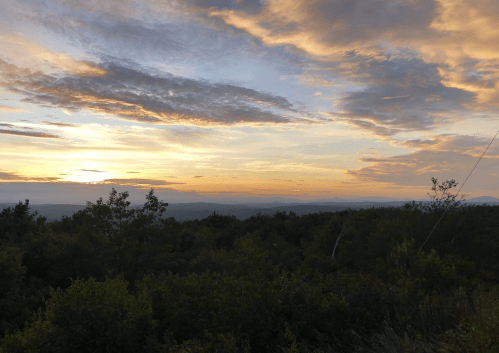 A scenic sunset over a lush landscape, with colorful clouds and distant mountains under a soft, glowing sky.