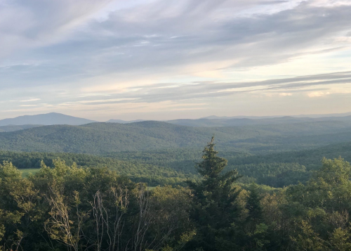 A panoramic view of rolling green hills and distant mountains under a cloudy sky.