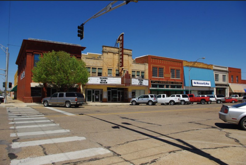 A small town street featuring historic buildings, a movie theater marquee, and parked cars under a clear blue sky.