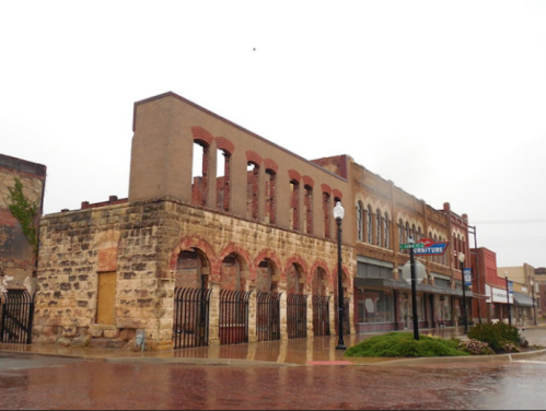 Historic buildings with brick facades, some partially ruined, in a small town on a rainy day.