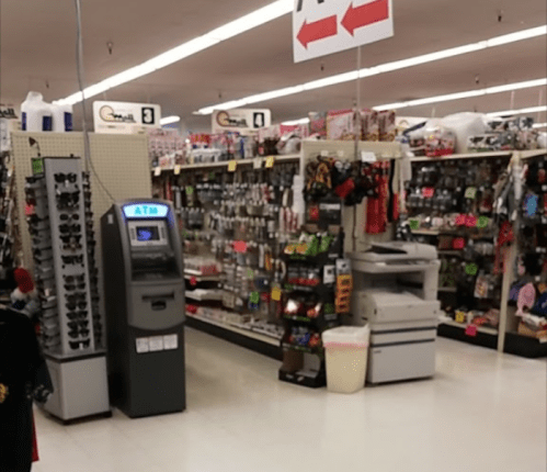 A store aisle filled with various products, featuring an ATM and a printer near the center.