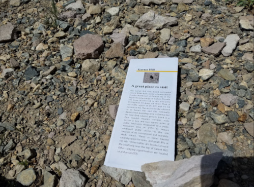 A brochure on the ground about Garnet Hill, surrounded by rocks and gravel.