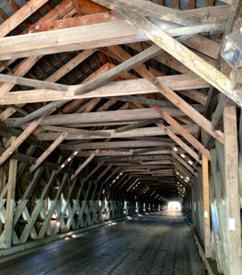 Interior view of a wooden covered bridge, showcasing exposed beams and a long, empty pathway leading to light.