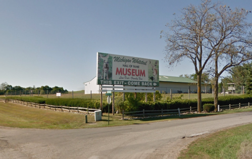 Sign for the Michigan Wildlife Hall of Fame Museum, with a grassy area and trees in the background.