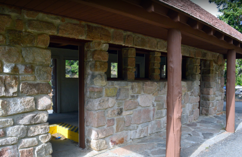 A stone building with wooden beams, featuring open windows and a pathway leading to the entrance.