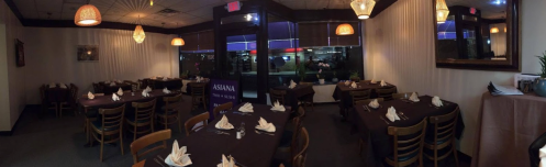 A panoramic view of a restaurant interior with tables set for dining, soft lighting, and a window showing the outside.