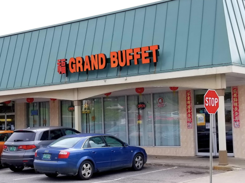 Exterior of a restaurant named "Grand Buffet," featuring a blue roof, open sign, and nearby stop sign.