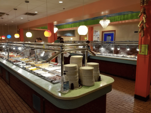 A bustling buffet with various food options, colorful lights, and diners serving themselves at the counter.
