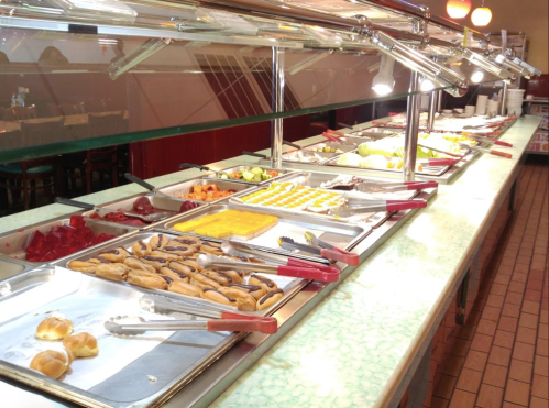 A buffet table with various dishes, including salads, desserts, and entrees, under bright lights.