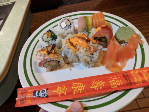 A plate of assorted sushi rolls, including salmon, crab, and avocado, with chopsticks and wasabi on the side.