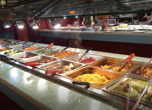 A buffet with various dishes in metal trays, including rice, vegetables, and meats, under bright lights.