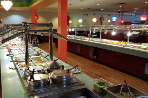 A buffet with various food dishes under metal covers, colorful decor, and a vibrant dining area in the background.