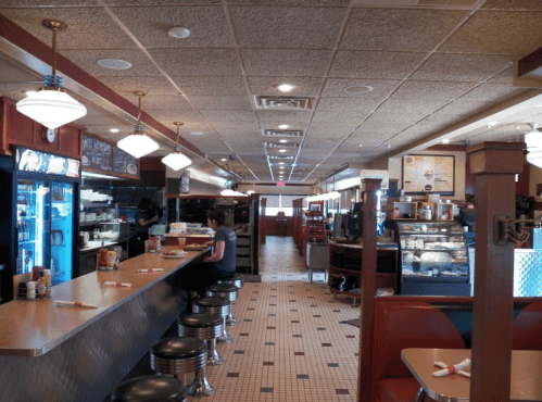 A diner interior featuring a long counter with stools, booths, and a display case, creating a cozy atmosphere.