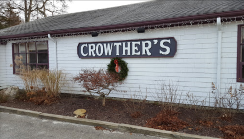 Sign reading "Crowther's" on a white building, decorated with a wreath and surrounded by winter landscaping.