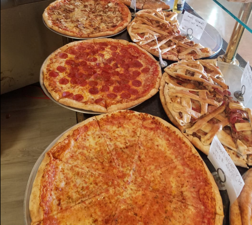A display of various pizzas, including pepperoni, cheese, and a dessert pizza, on metal trays.