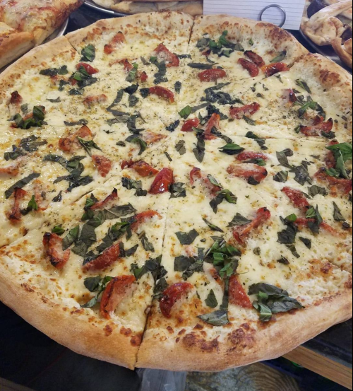 A large pizza topped with cheese, sun-dried tomatoes, and fresh basil on a golden crust.