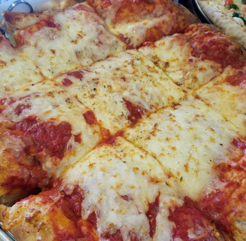 A close-up of a rectangular pizza with a golden cheese topping and tomato sauce, cut into square slices.