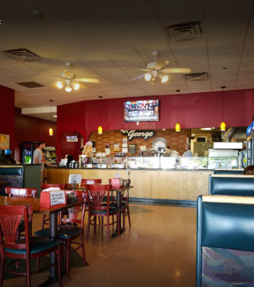 Interior of a casual restaurant with red walls, wooden counter, tables, and a TV displaying sports.