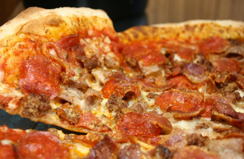 A close-up of a slice of pizza topped with pepperoni, sausage, and melted cheese, with a crispy crust.