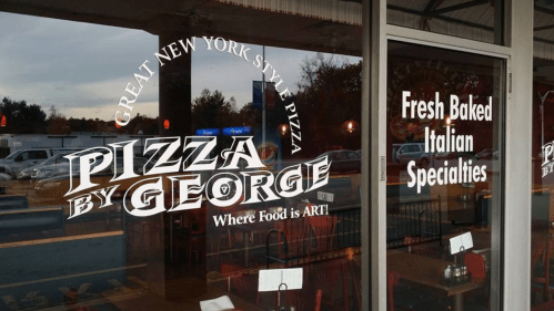 Window display of "Pizza by George," featuring text about New York-style pizza and Italian specialties.