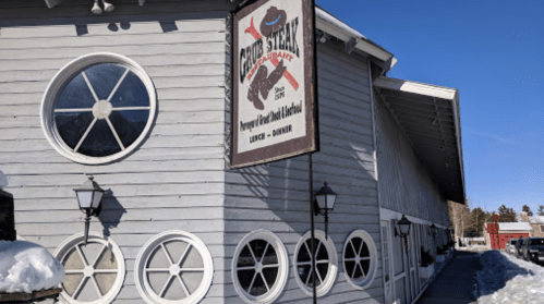 Sign for "Grizzly Restaurant" on a wooden building with circular windows, surrounded by snow and clear blue sky.