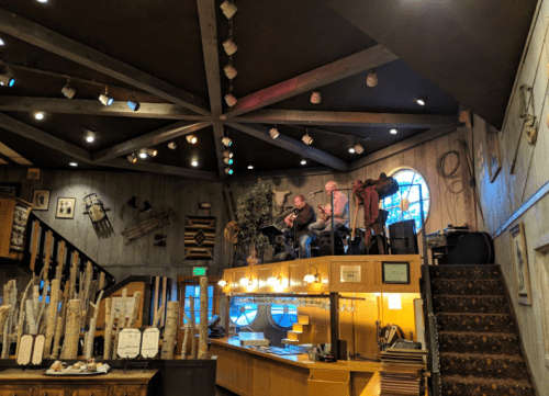 A cozy restaurant interior with musicians performing on a raised platform, surrounded by rustic decor and warm lighting.
