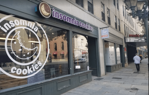 Exterior of Insomnia Cookies shop with large window display, located on a city street. A person walks by.