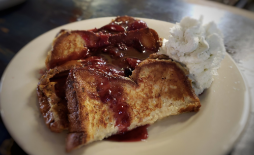 A plate of French toast topped with berry sauce and a dollop of whipped cream.
