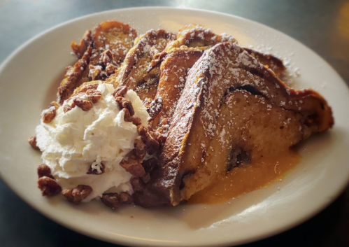 A plate of French toast topped with powdered sugar, served with whipped cream and chopped nuts on the side.