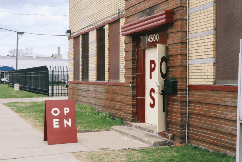 A brick building with an open door and a sign reading "OPEN" on the sidewalk.