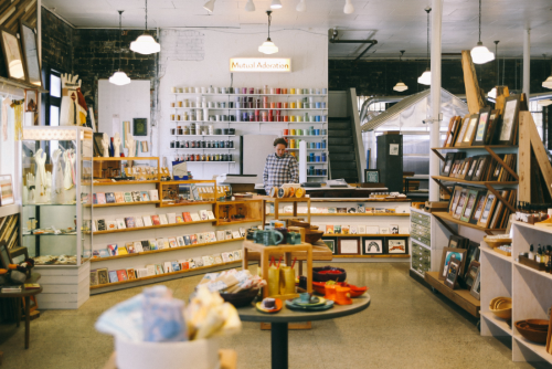 A cozy shop interior with shelves of colorful items, cards, and crafts, featuring a person at the counter.