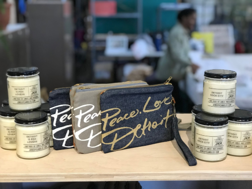 A display of candles and denim pouches with "Peace, Love, Detroit" text on a wooden shelf.