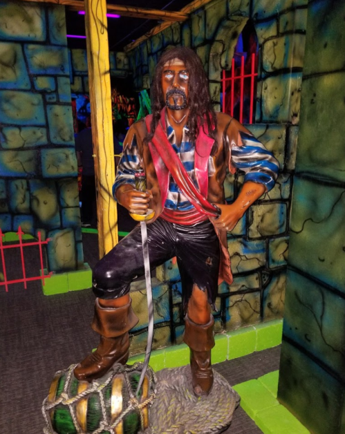 A life-sized pirate statue stands confidently, holding a sword, against a colorful, themed backdrop.