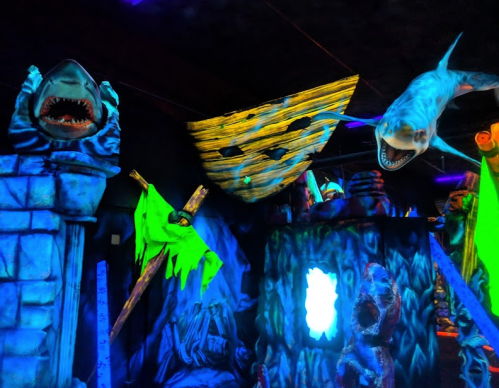 A vibrant, neon-lit indoor scene featuring shark sculptures and eerie decorations in a dark environment.
