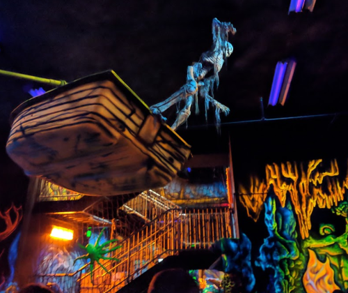 A spooky, dimly lit room with glowing decorations, featuring a skeleton hanging from a boat above a staircase.