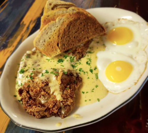 A plate of fried chicken with creamy gravy, two sunny-side-up eggs, and slices of toasted bread.