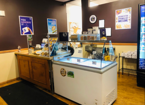 A dessert counter featuring a freezer, snacks, and promotional signs in a cozy shop setting.