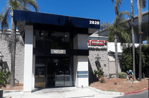 Exterior of a restaurant building with a modern design, featuring large windows and palm trees in the surroundings.