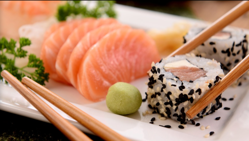 A plate of sushi featuring salmon sashimi, sushi rolls with sesame seeds, wasabi, and garnished with parsley.
