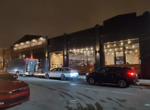 A dimly lit street scene featuring a building with "PHS Mechanical Company" signage and parked cars outside.
